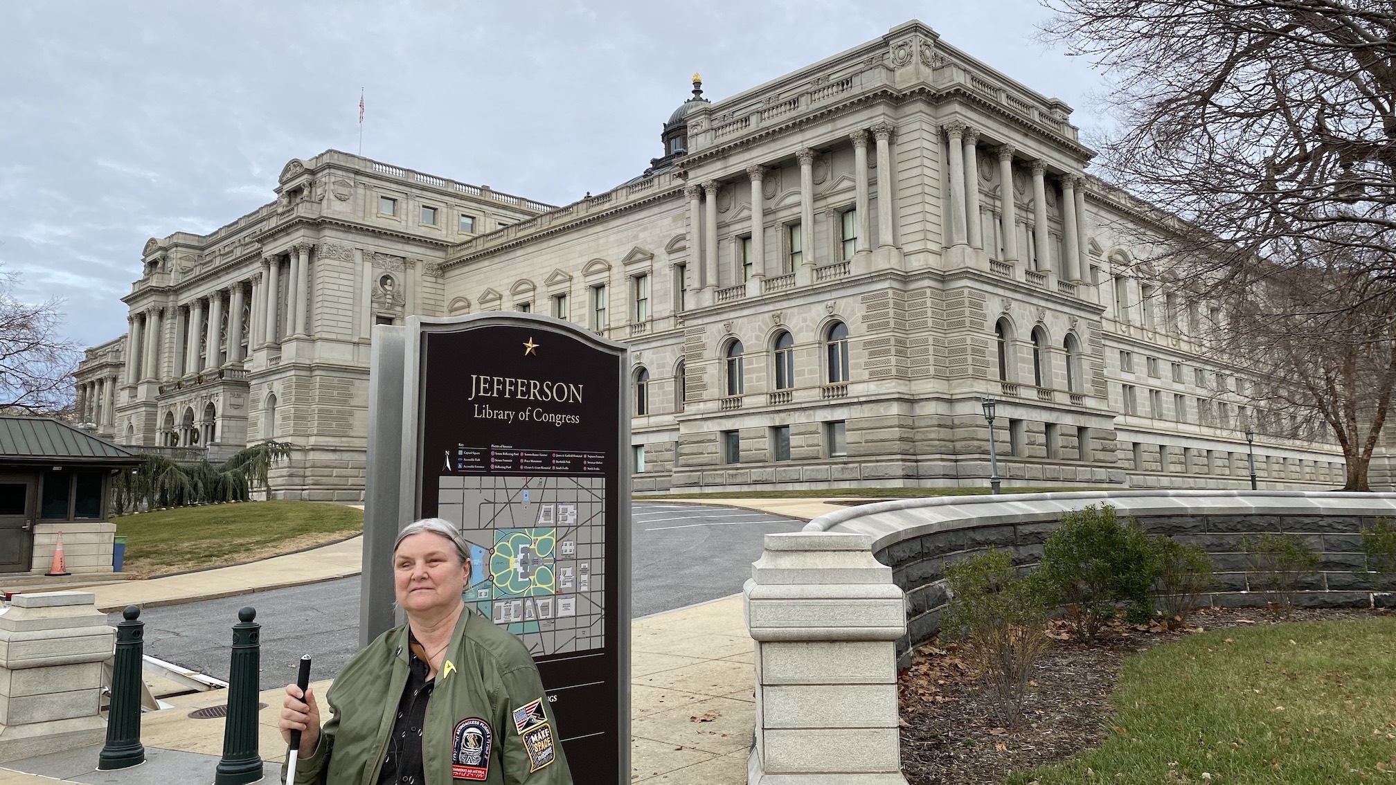 Photo of Dr. Wells-Jensen standing in front of the Library of Congress Jefferson Building, holding a white cane and wearing an AstroAccess flight jacket.